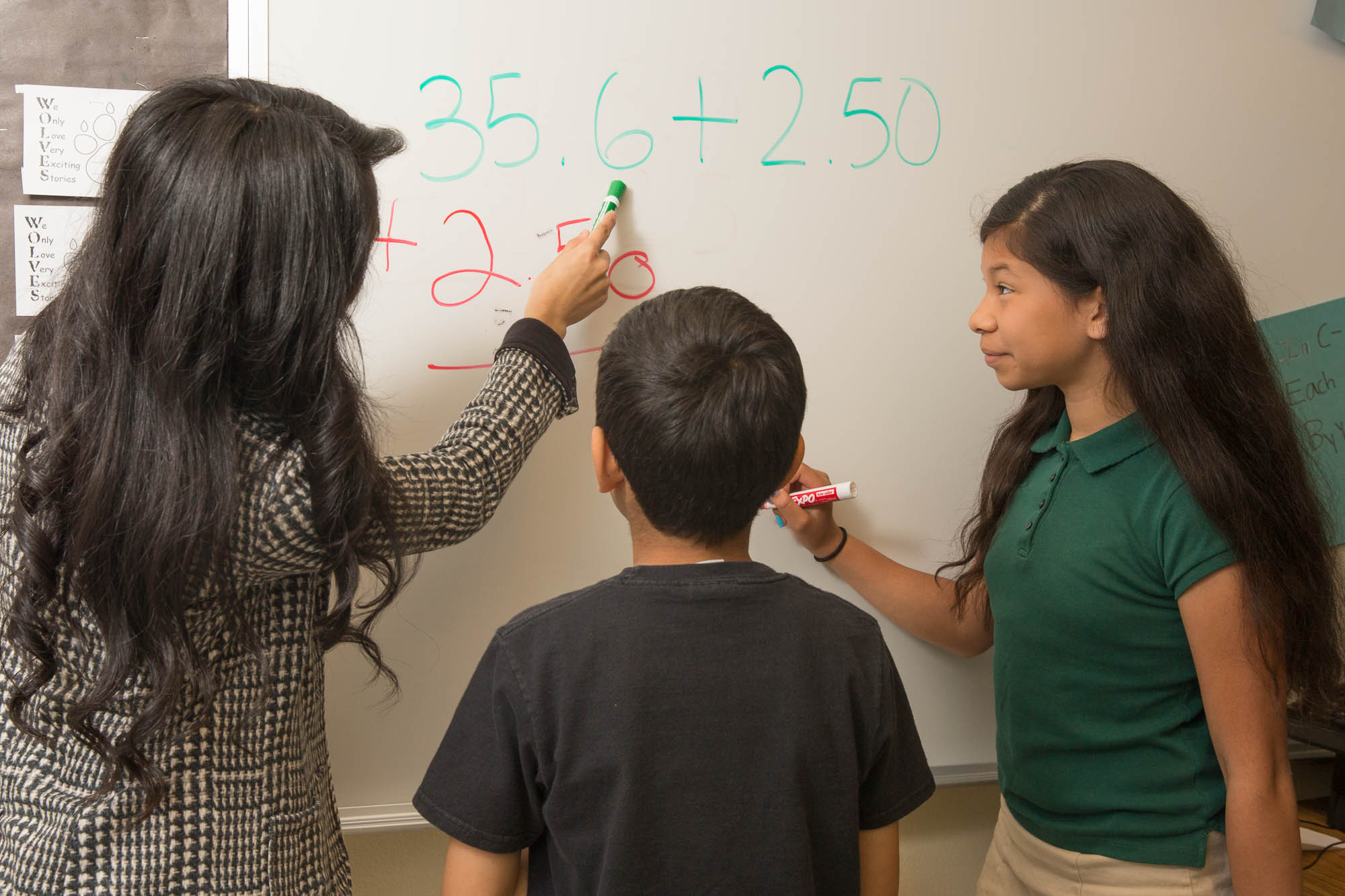 A teacher working on math with two children on a whiteboard.